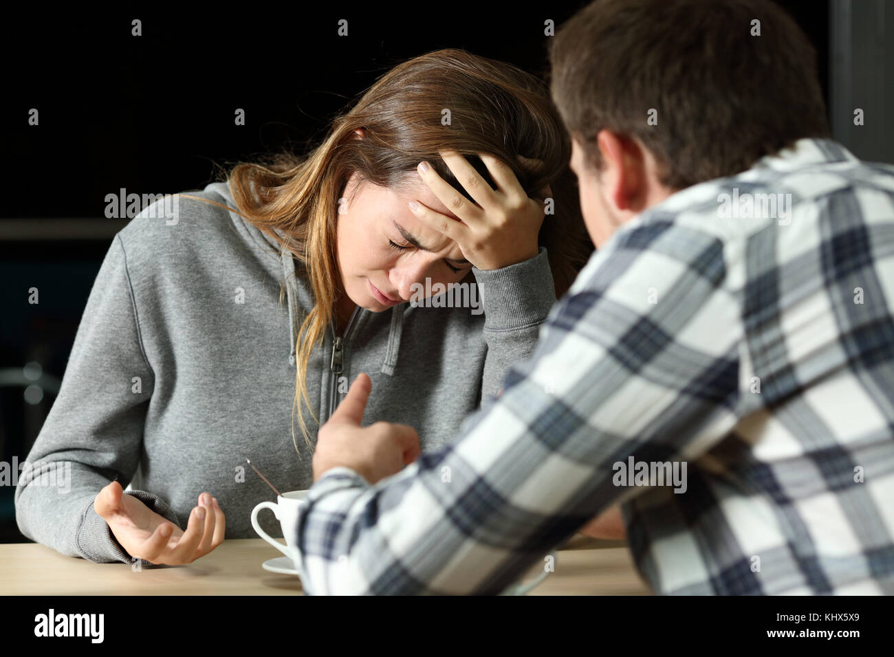 Sad teenager crying during a couple fight in a coffee shop in the night Stock Photo