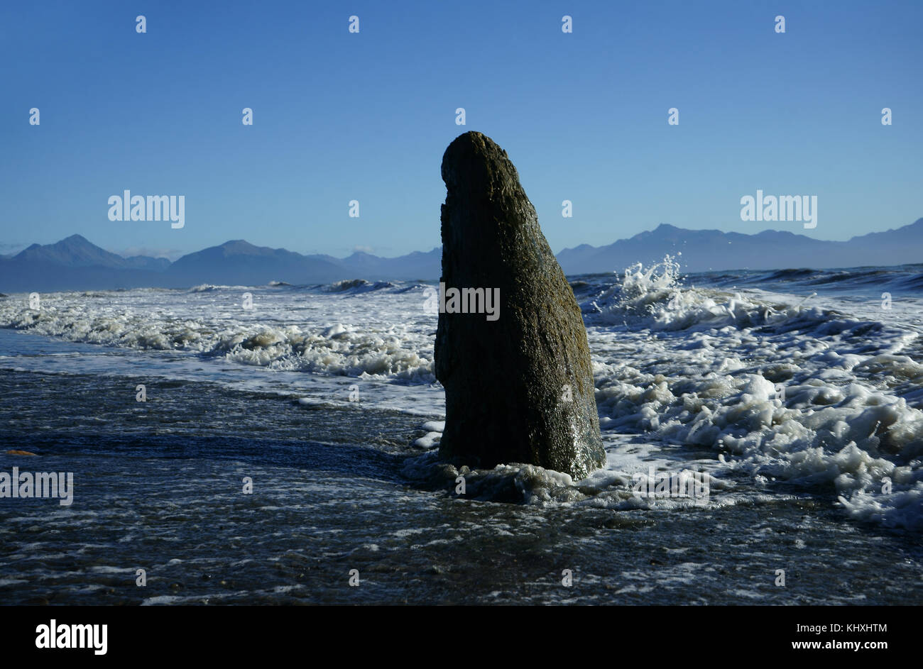 Long rock stcking our of tidal sand beach with waves, Kachemak Bay, Cook Inlet, Kenai Peninsula, Alaska Stock Photo