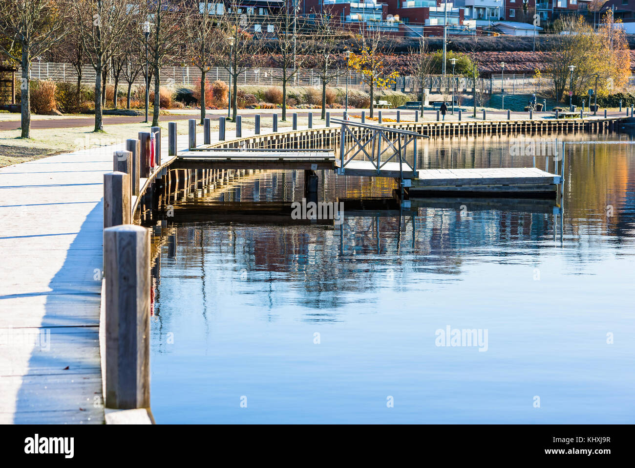 Wooden combo pier with three sections. A normal pier with a bridge and railings and the last part is a floating pier. Water is calm and the boardwalk  Stock Photo