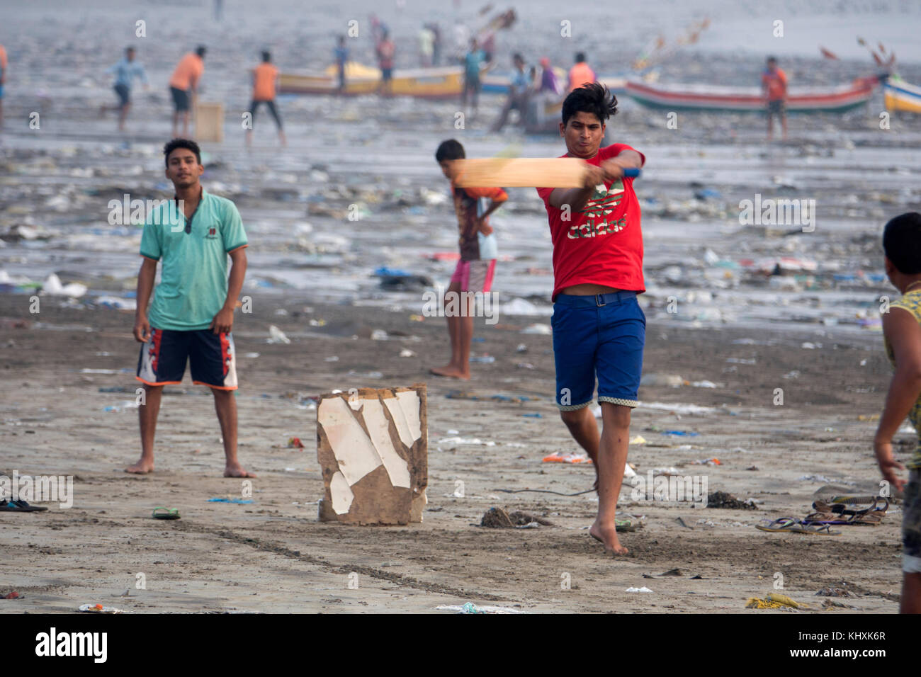 Indian teenage boys playing game of cricket among plastic garbage and other rubbish on Versova Beach, Mumbai Stock Photo