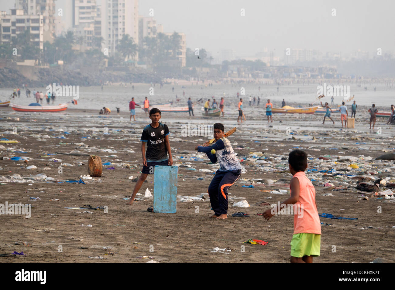Children playing game of cricket among plastic garbage and other rubbish on Versova Beach, Mumbai, India Stock Photo