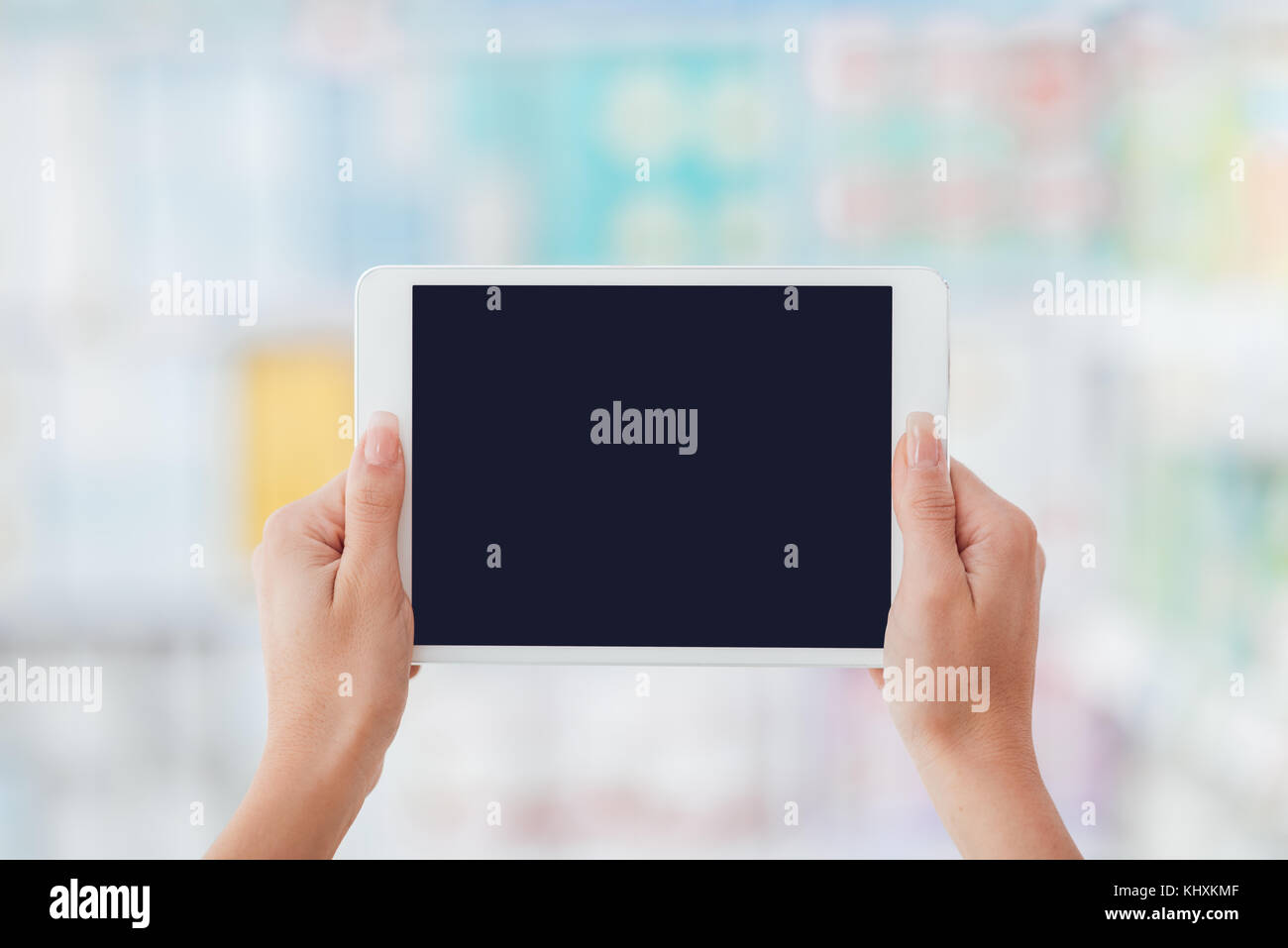Female hands holding a digital touch screen tablet, supermarket shelves ...