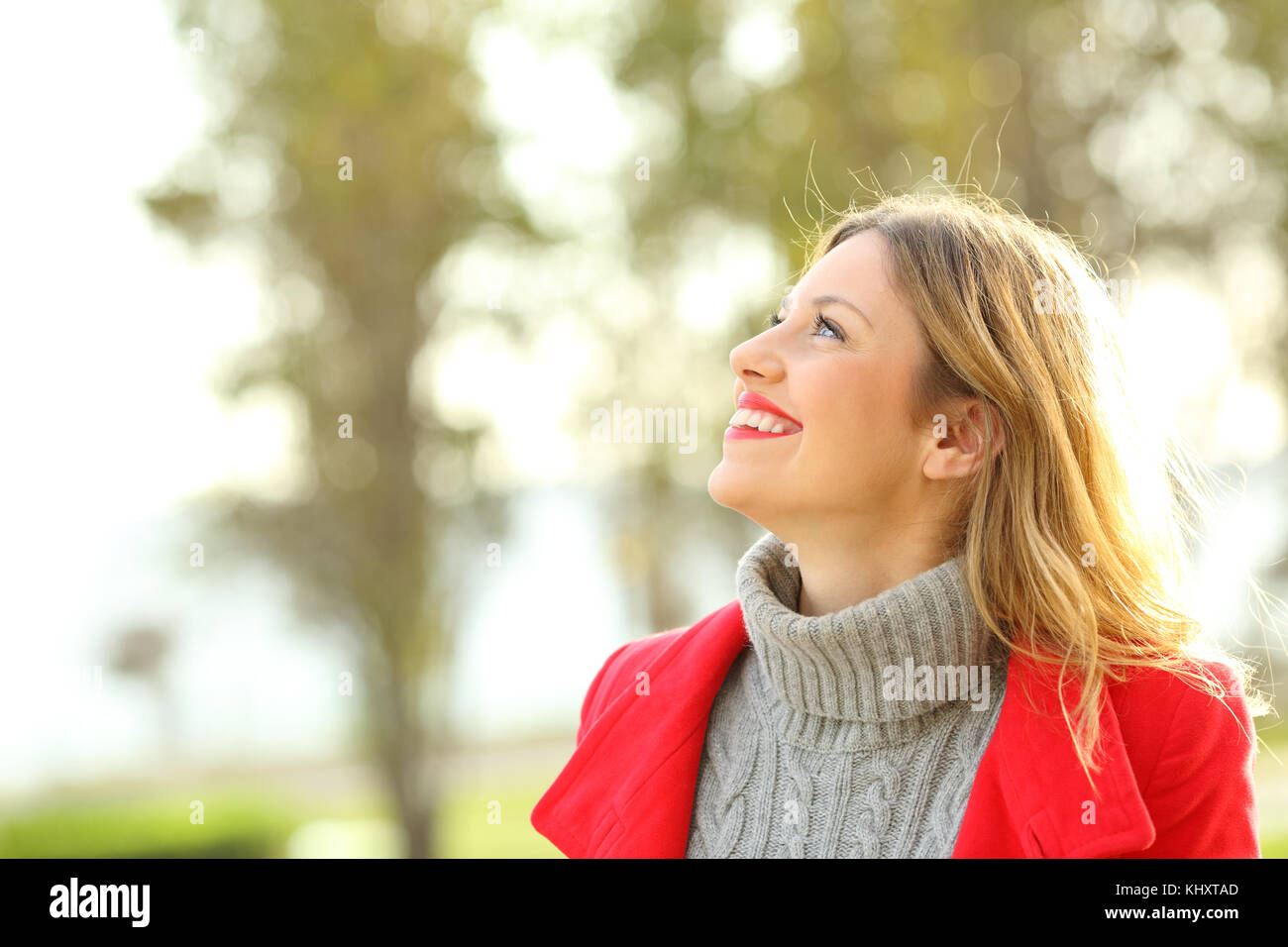 Profile of a happy fashion woman wearing a red jacket looking above in winter Stock Photo