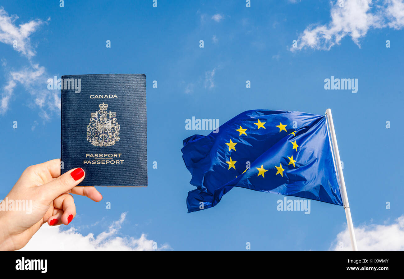 European Union (EU) flag against a blue sky with digital composite of woman holding a Canadian passport Stock Photo