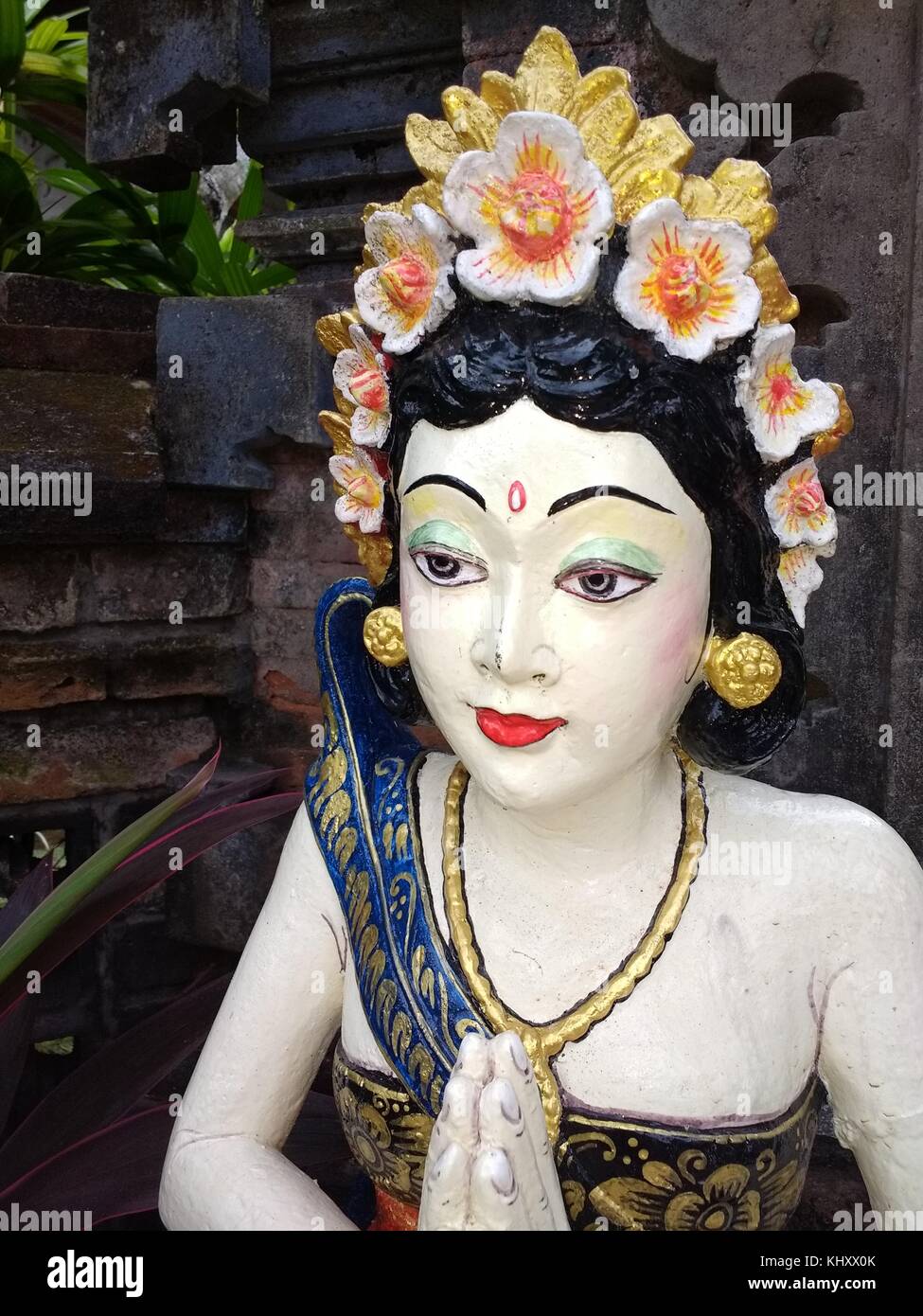 Close up of brightly painted statue of female worshipper praying in traditional dress with beautiful frangipani headdress on island of Bali, Indonesia Stock Photo