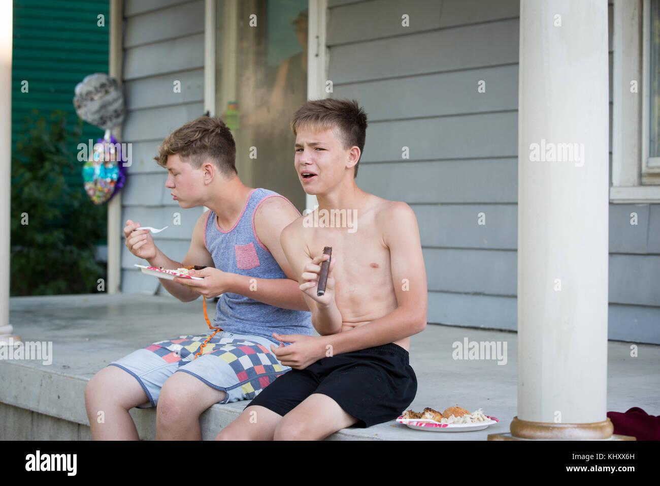 Two teenage boys sitting on porch, eating and smoking cigar Stock Photo