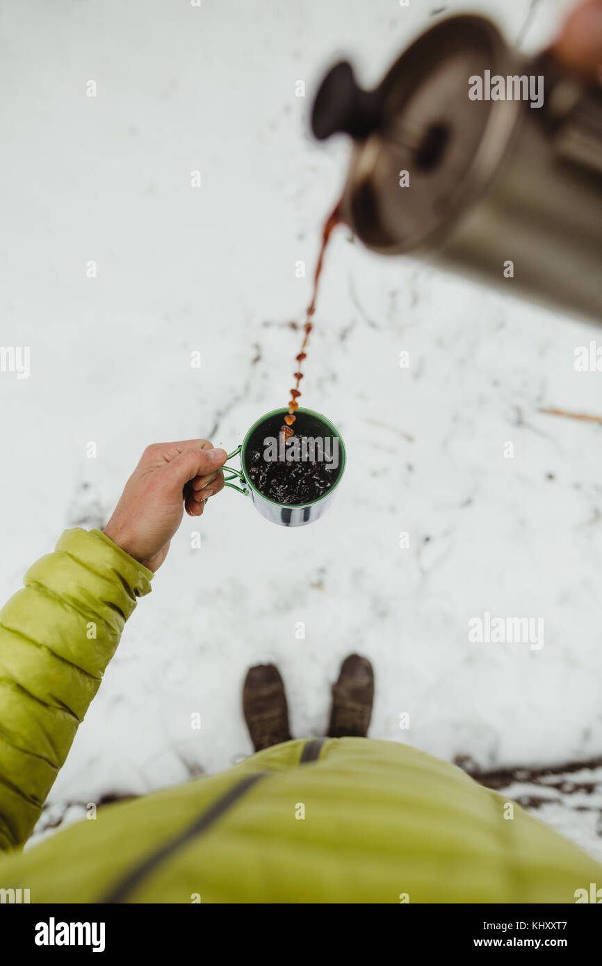 Personal perspective view of male hiker pouring coffee from flask in snow Stock Photo