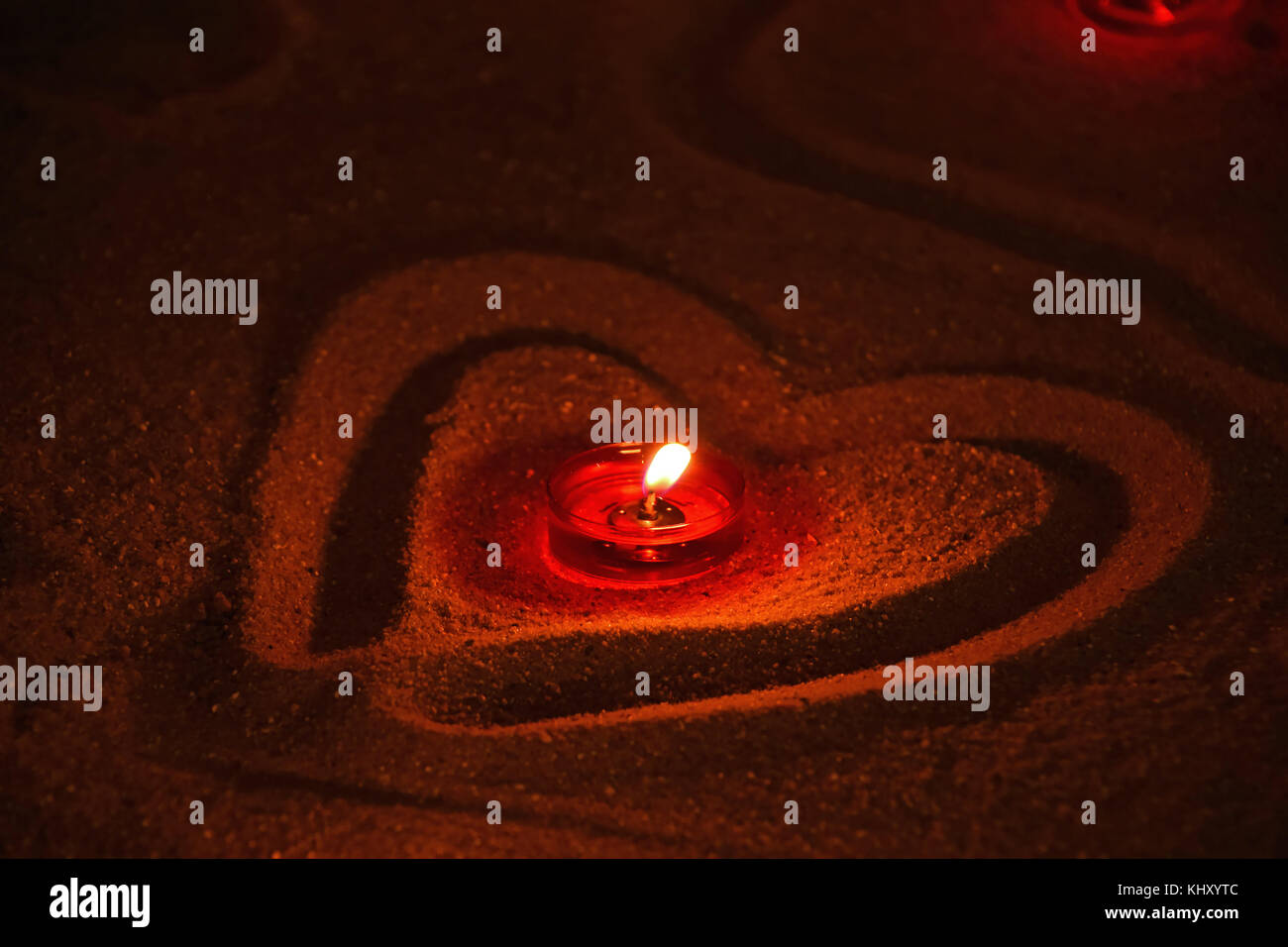 Red church tea candle burning in heart shaped sand, close up, high angle view Stock Photo