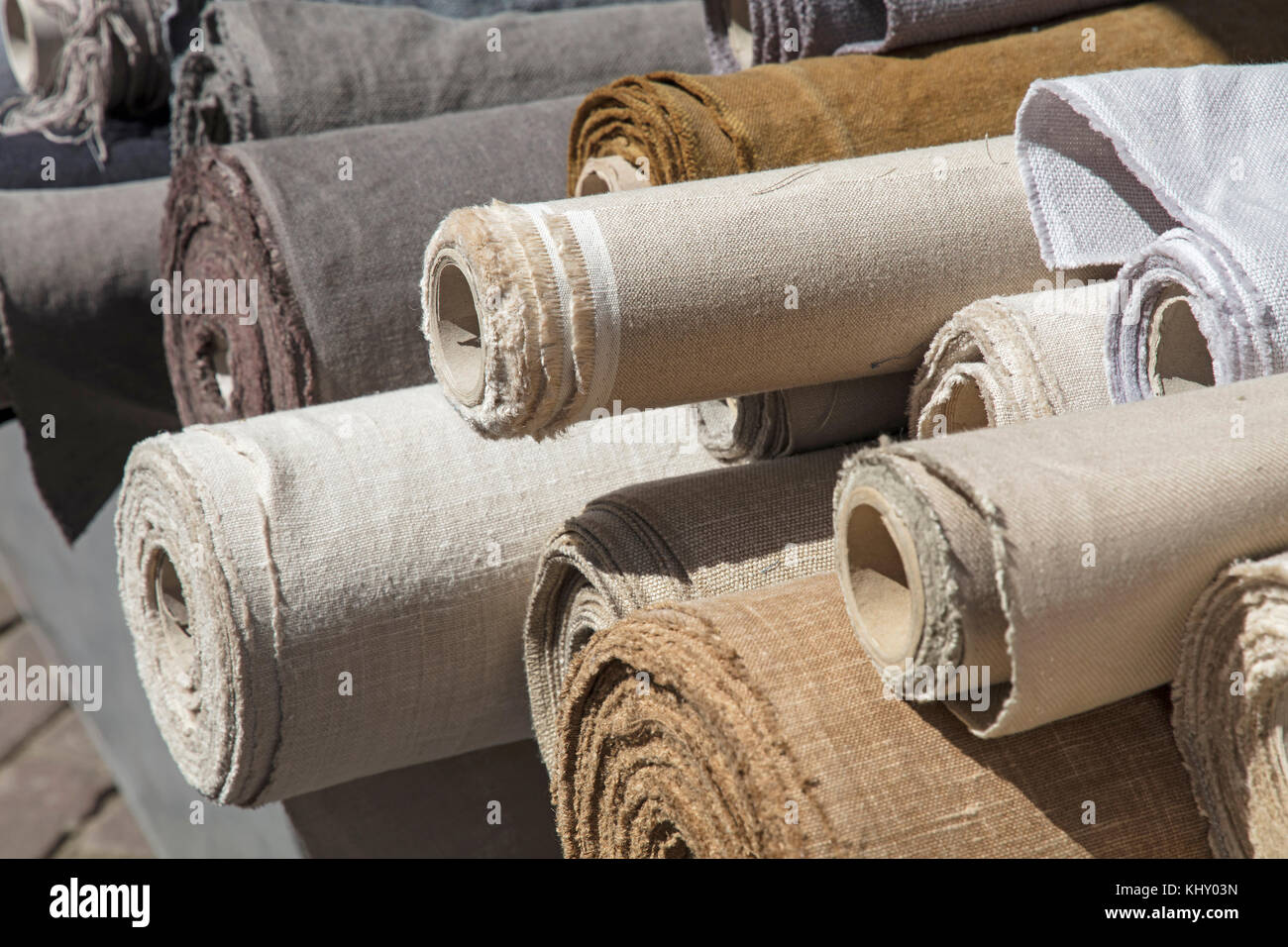 Close up assorted rolls of white, beige and brown flax linen fabric and canvas textile on retail market stall, high angle view Stock Photo