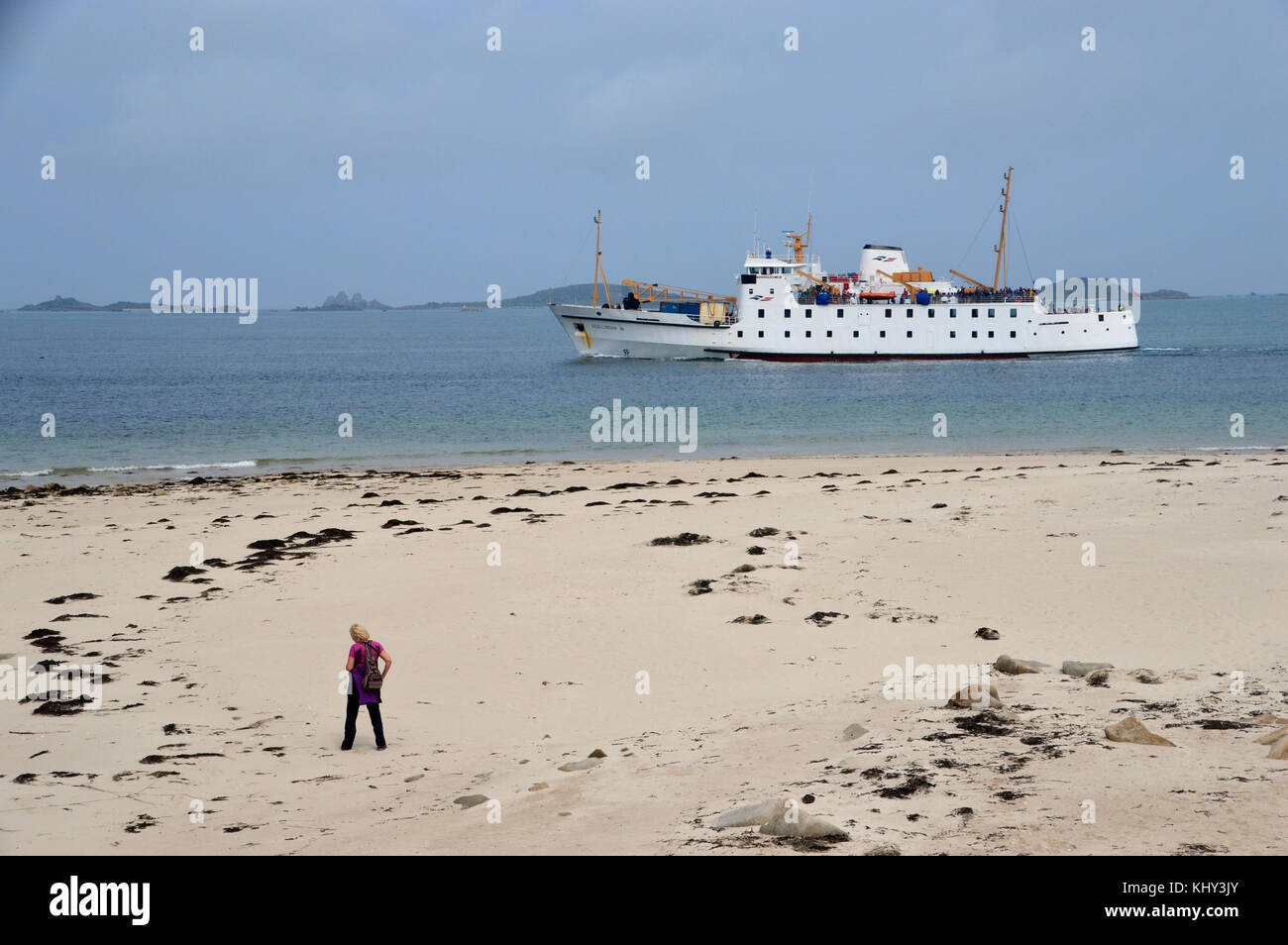 Lone Woman Walking on Bar Point Beach as the RMV Scillonian III Ferry passes en-route from Penzance to St Mary's, Isles of Scilly, Cornwall, UK. Stock Photo