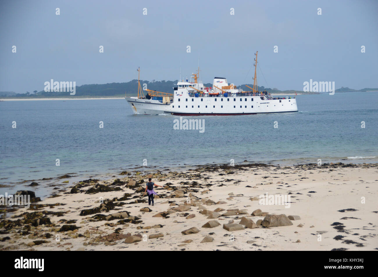 Lone Woman Walking on Bar Point Beach as the RMV Scillonian III Ferry passes en-route from Penzance to St Mary's, Isles of Scilly, Cornwall, UK. Stock Photo