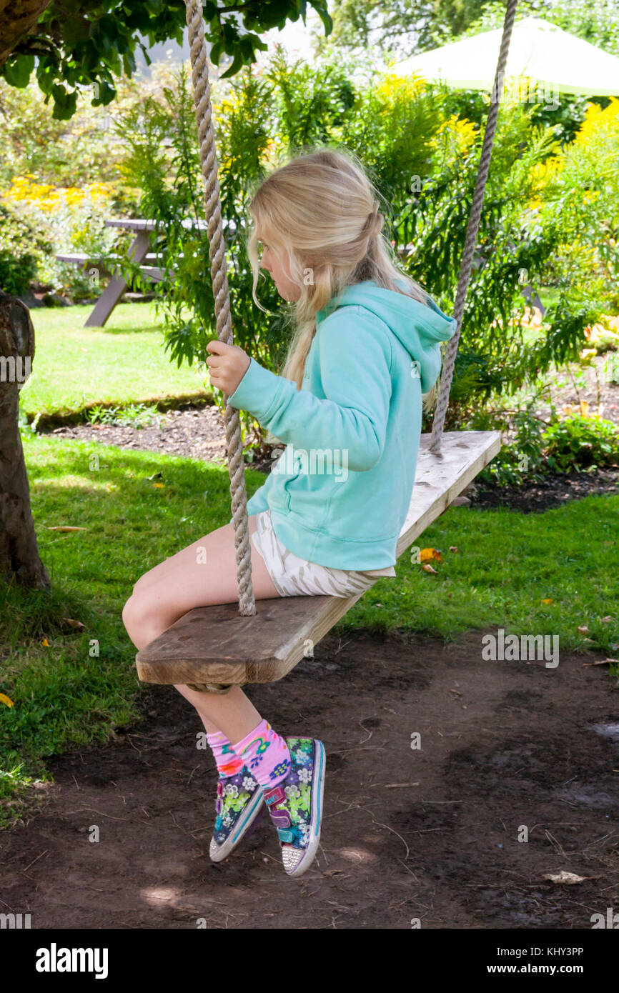 Blonde child, kid swinging on a tree swing in a lush green garden with trees  and bushes on a sunny summers day, Ireland Stock Photo - Alamy