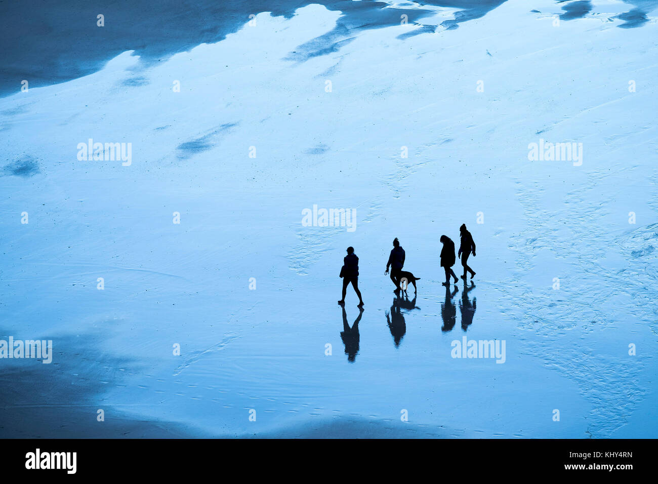 People figures seen in silhouette walking across a beach in early morning light. Stock Photo