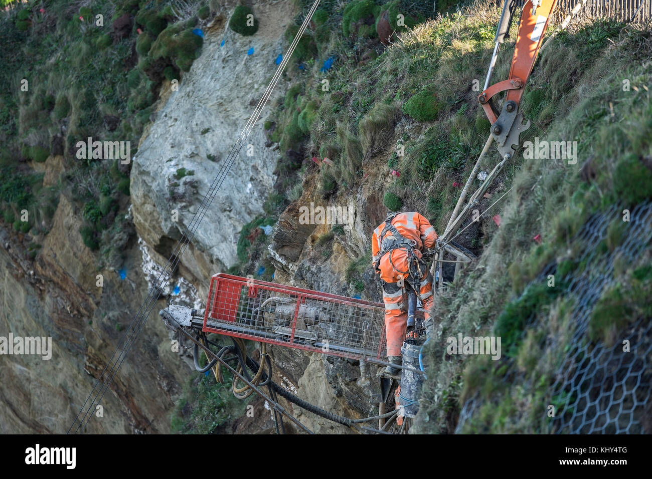 Two workers drilling holes in an unstable cliff above Tolcarne Beach in Newquay Cornwall UK