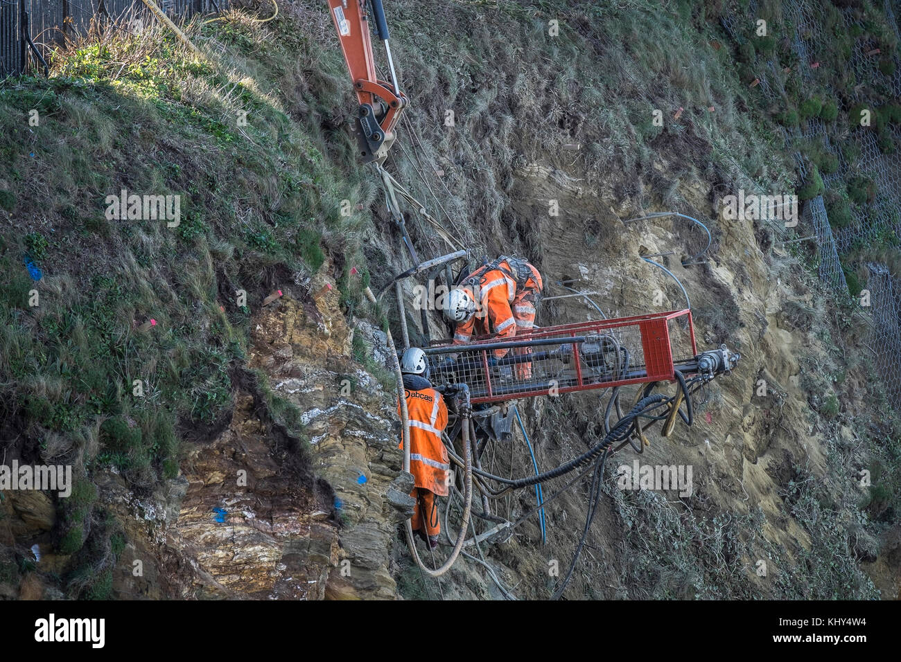 Two workers drilling holes in an unstable cliff above Tolcarne Beach in Newquay Cornwall UK. Stock Photo