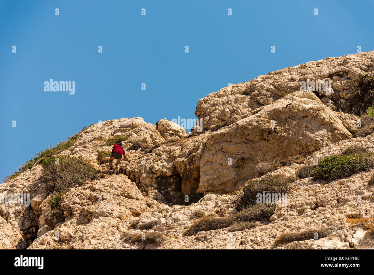 A woman climbing on top of Aphrodite Rock in Cyprus between Limassol