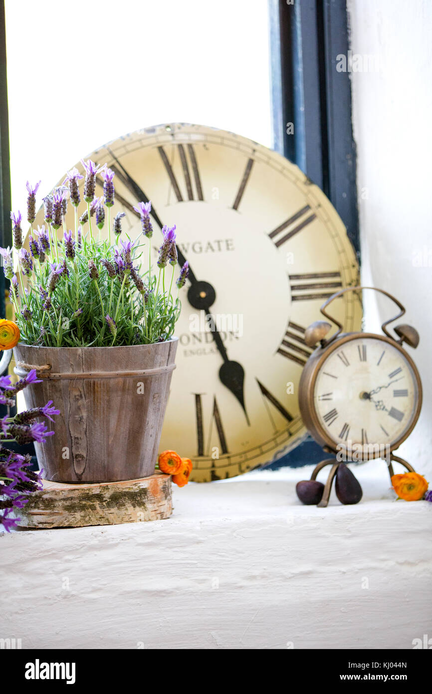 Still life of lavender plant, vintage clock face and alarm clock on windowsill Stock Photo