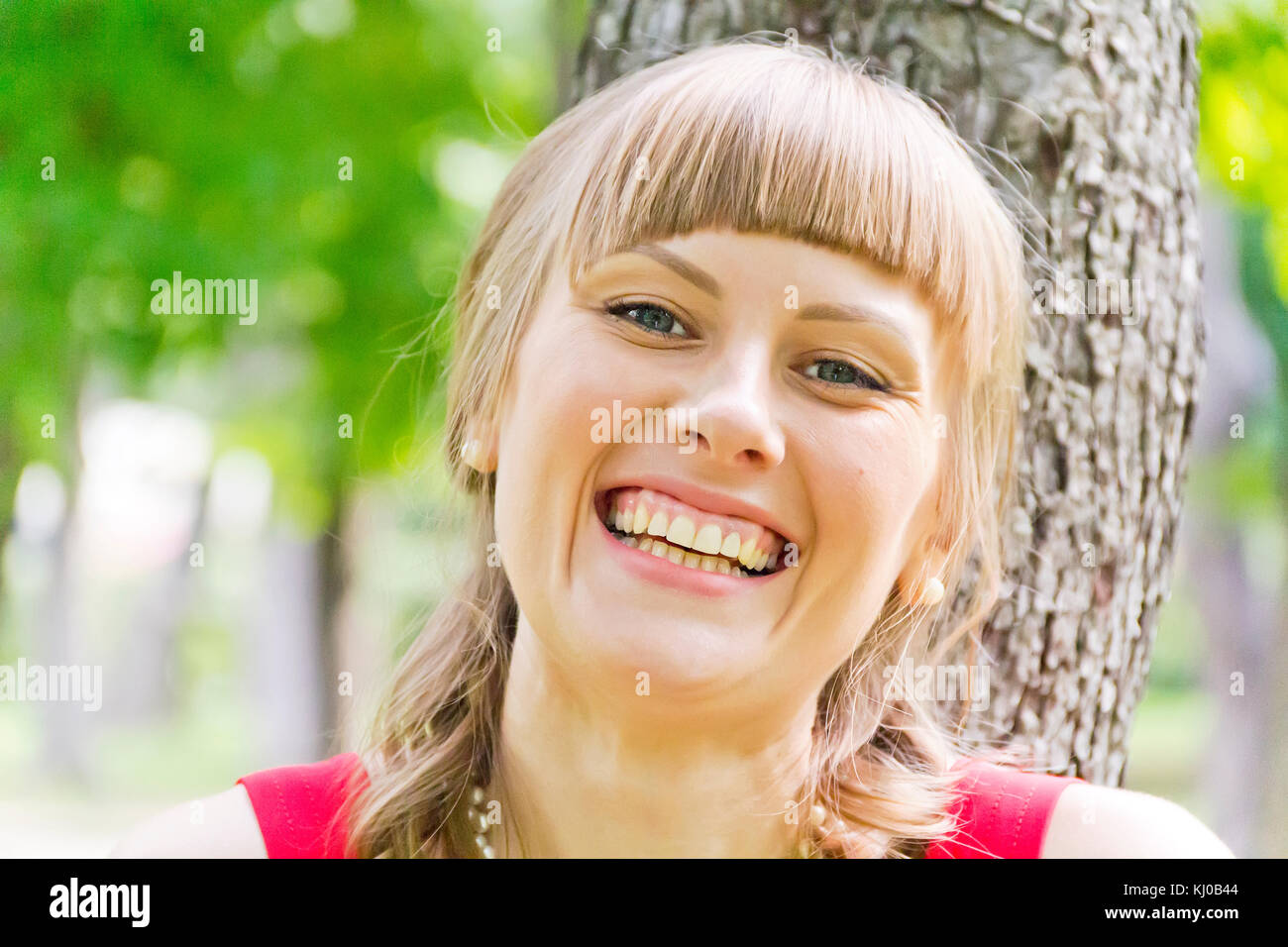 Portrait of smiling blond girl on green wood background Stock Photo - Alamy