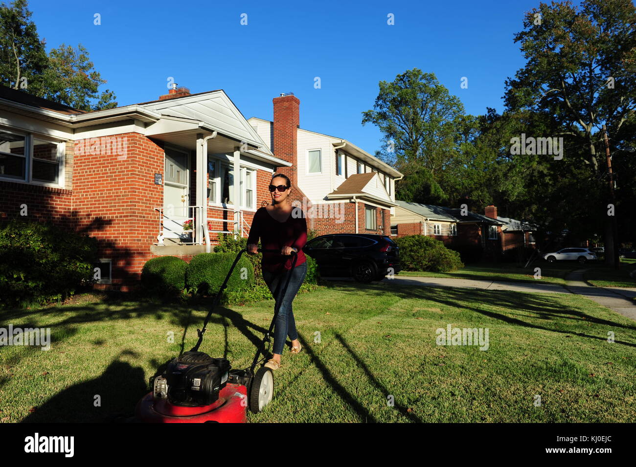 Hispanic woman mowing her lawn in suburban Maryland MD USA Garret Park Stock Photo