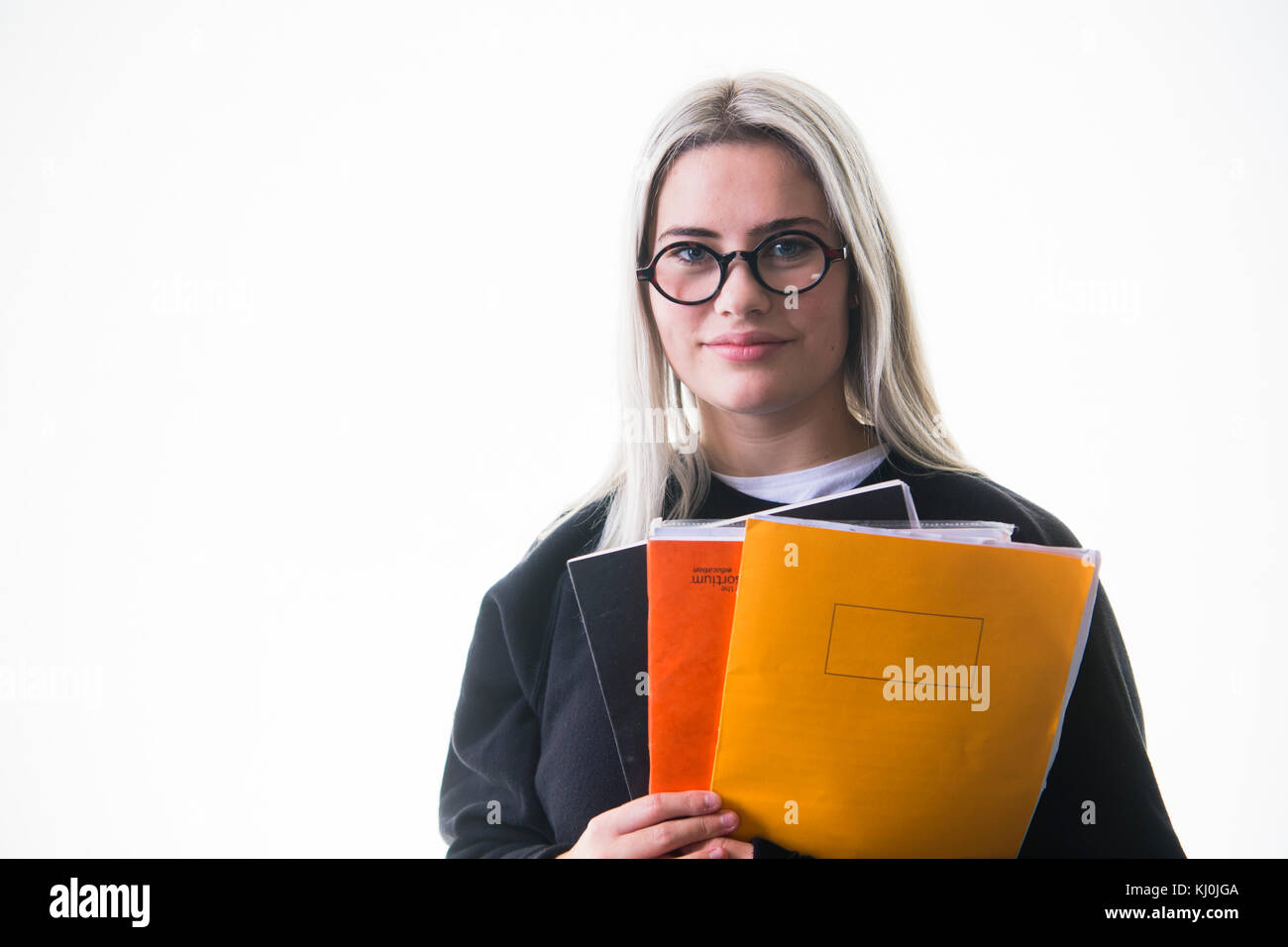 Secondary education in the UK: A young teenage girl, 16, 17 years old, student pupil wearing glasses, going to school college with her notebooks work homework in her arms, UK Stock Photo