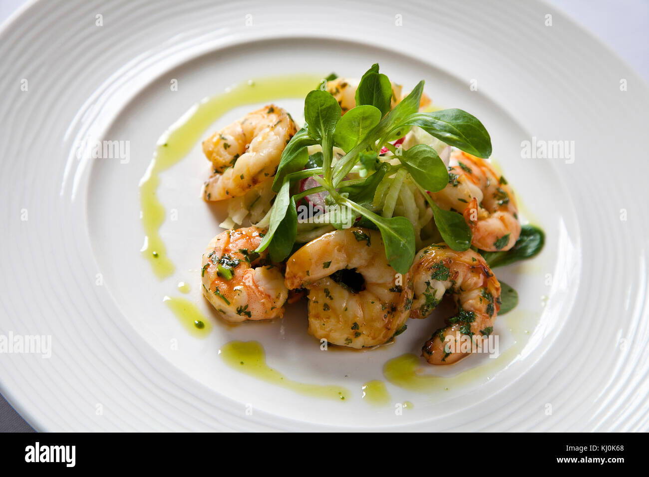 King prawns in garlic and herbs with green cress on white plate Stock Photo