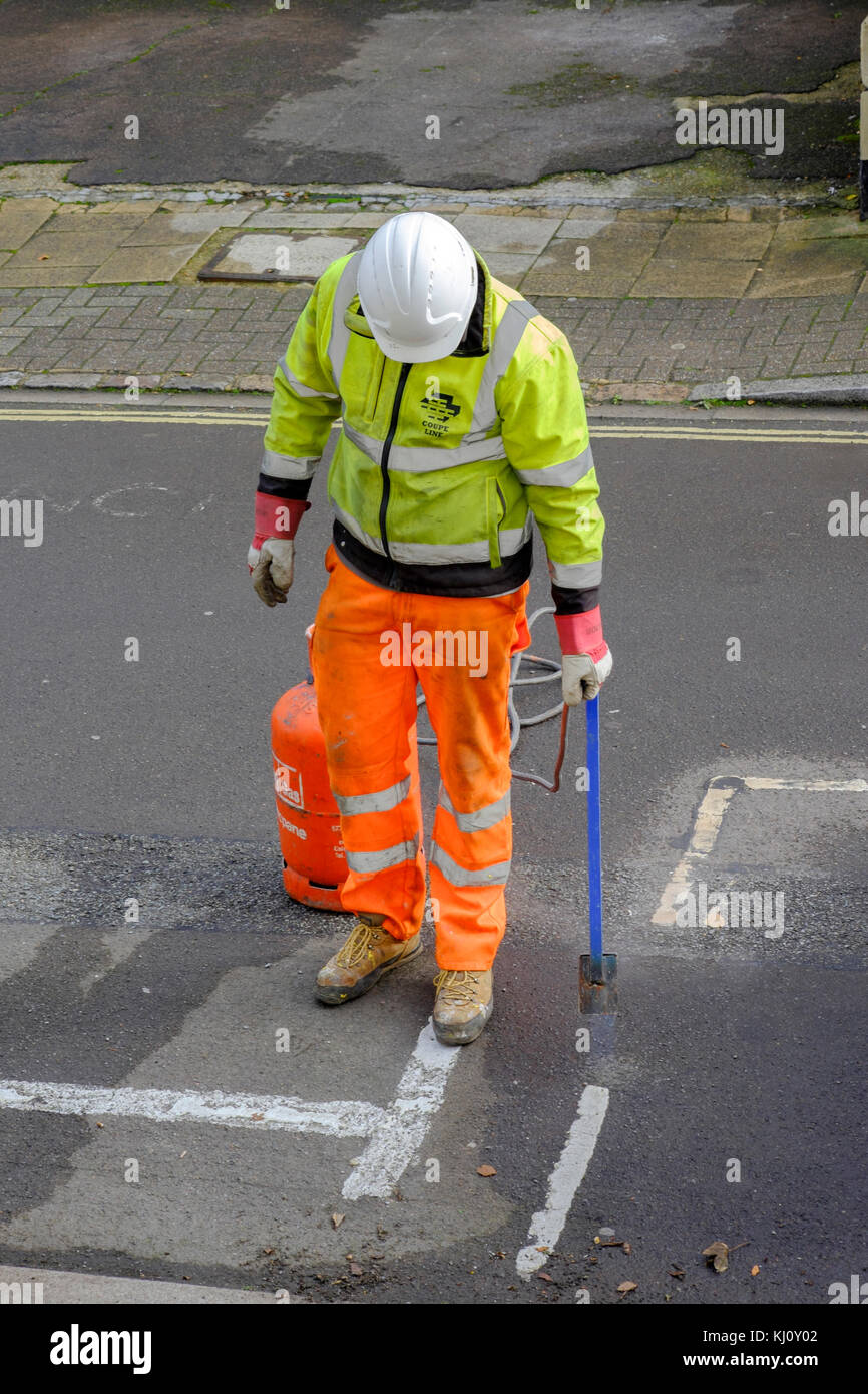 male worker wearing high visibility clothing burning off old road markings with a flame gun england uk Stock Photo