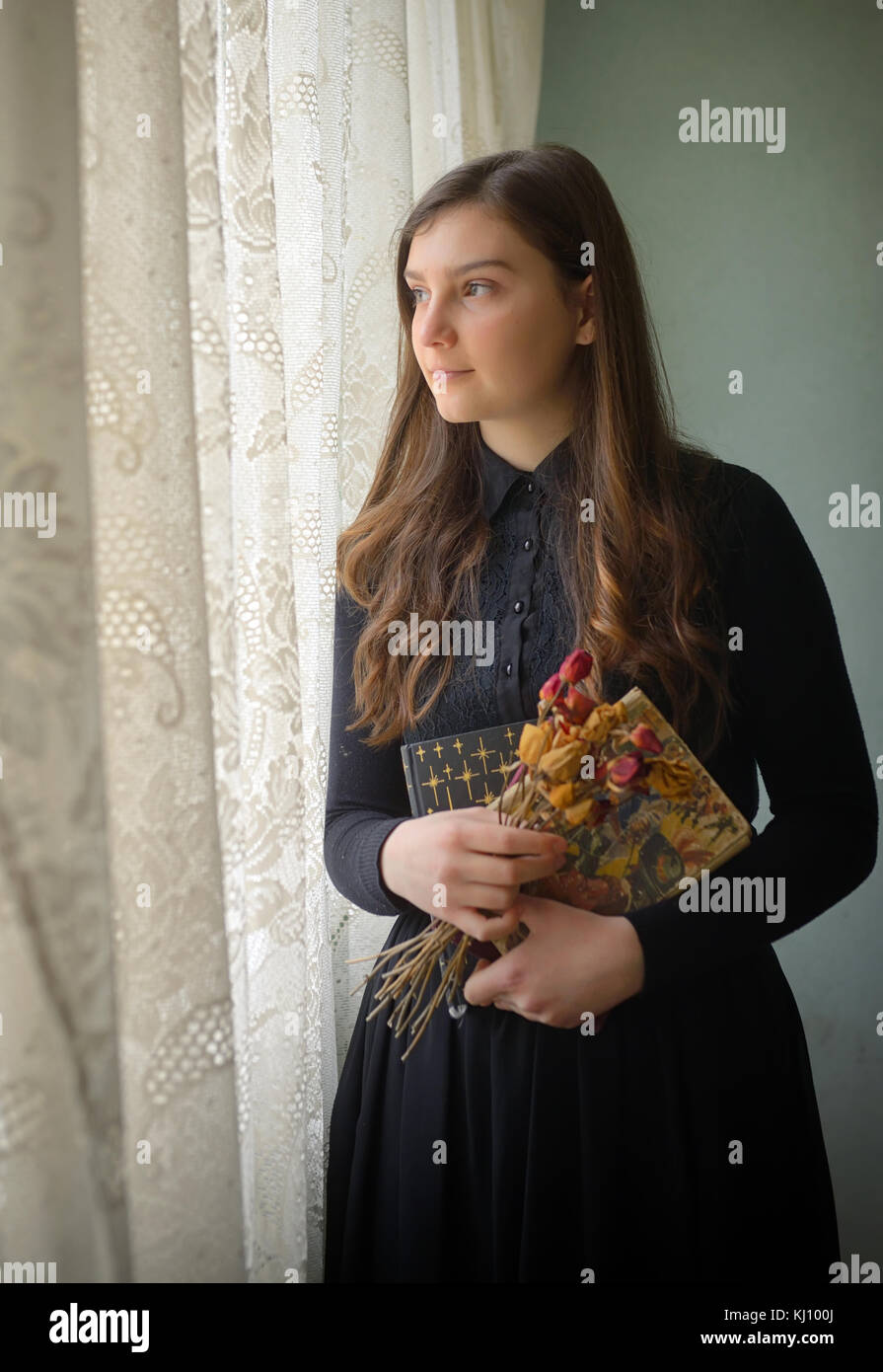Young girl in black vintage dress standing near window Stock Photo