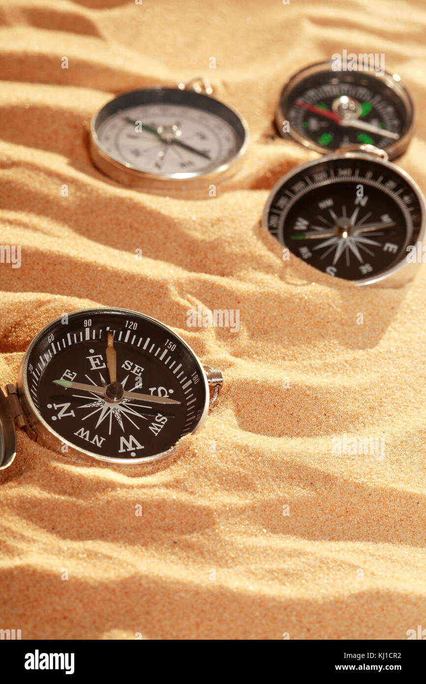 Conceptual background with few compasses lying on sand. Vertical image Stock Photo