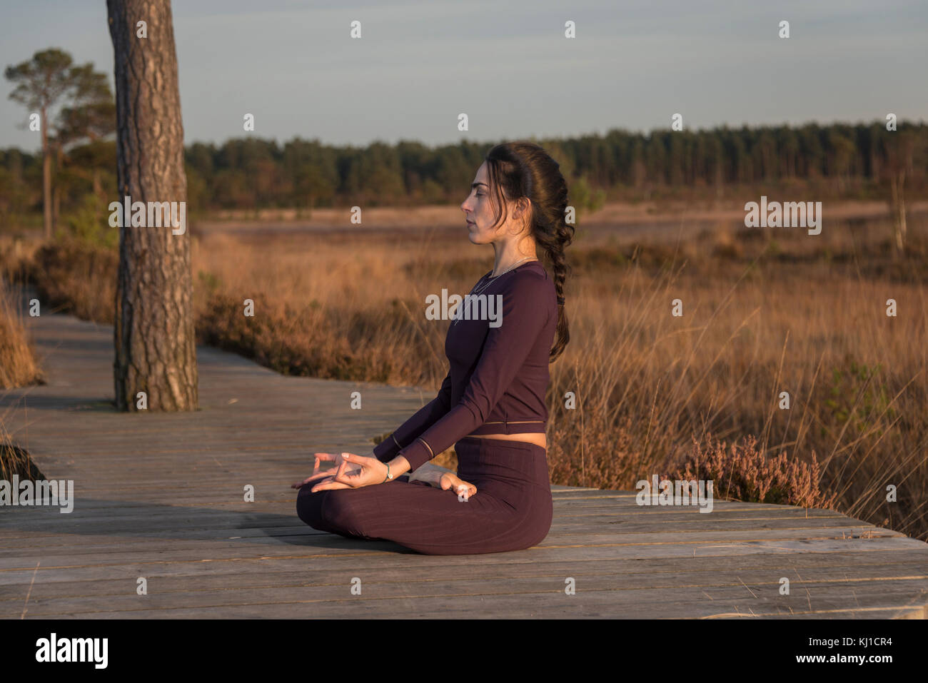 woman practicing yoga outside in open space in a nature reserve, seated lotus position. Stock Photo
