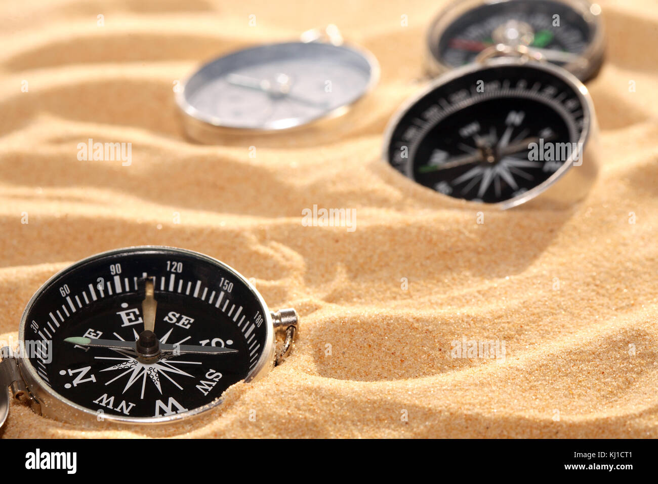 Conceptual background with few compasses lying on sand. Horizontal image Stock Photo