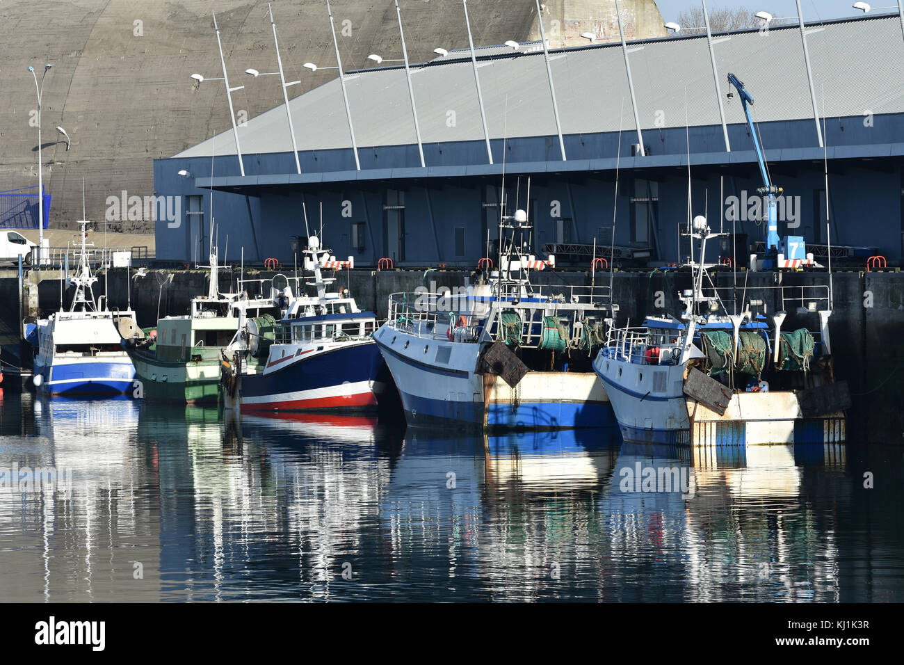 Fishing boats docked at Keroman wharf, Lorient, Brittany, France. Horizontal three-quarter stern view with warehouse in background Stock Photo