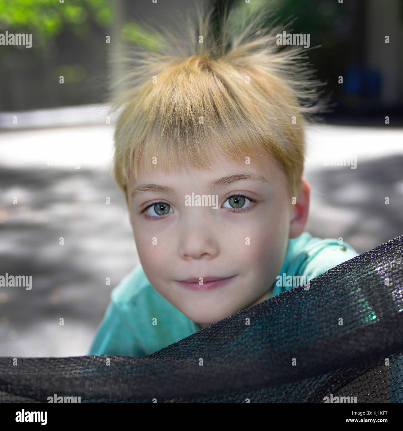 Portrait of Handsome, Young Caucasian boy with blond hair sticking up from static electricity outside on trampoline Stock Photo