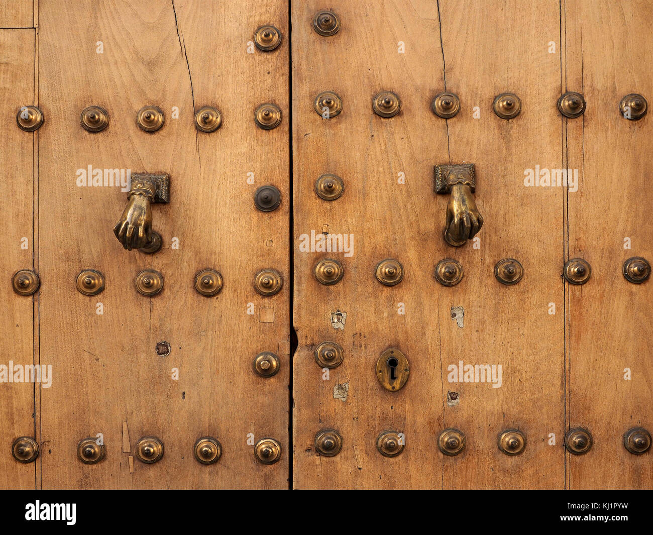 ancient studded wooden door with rows of brass studs and pair of brass door knockers in shape of hands in Ronda,Spain Stock Photo