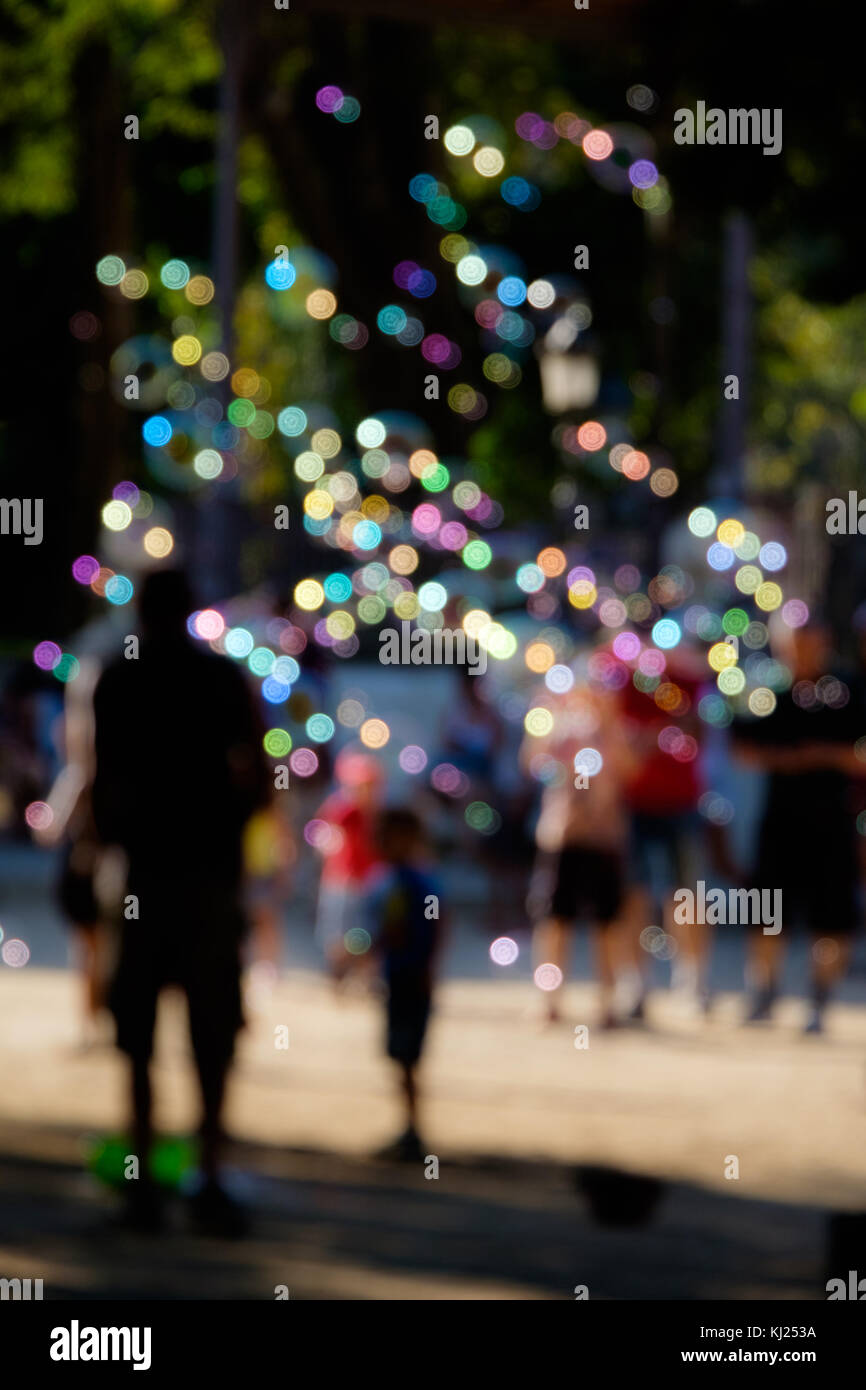 People walking around Parc de la ciutadella while a man is creating hundreds of colorfull bubbles Stock Photo