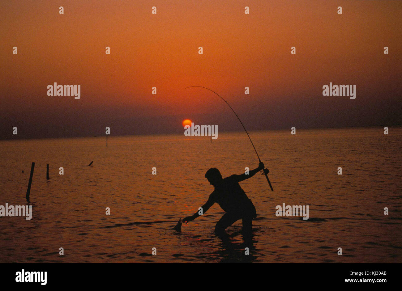 Silhouette of fisherman on the sea water in sunset Stock Photo - Alamy
