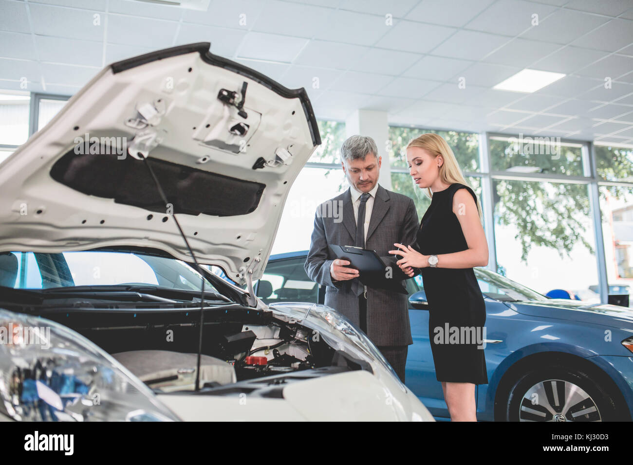 Auto dealer showing motor of electric car to young woman. Stock Photo