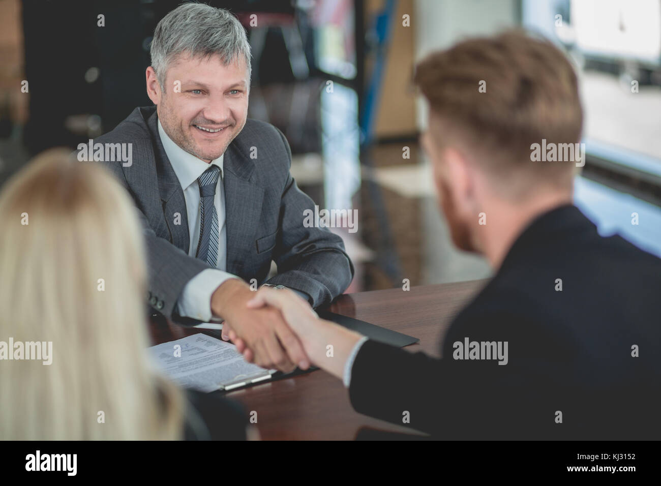 Auto dealer agent signing purchasing contract with a buyer, shaking hands. Stock Photo