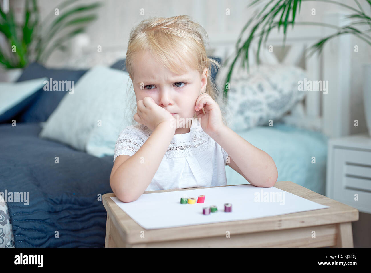 Sulky grumpy attractive little blond girl sitting with paper and crayons at  a small wooden desk staring off to the side with her chin on her hand Stock  Photo - Alamy