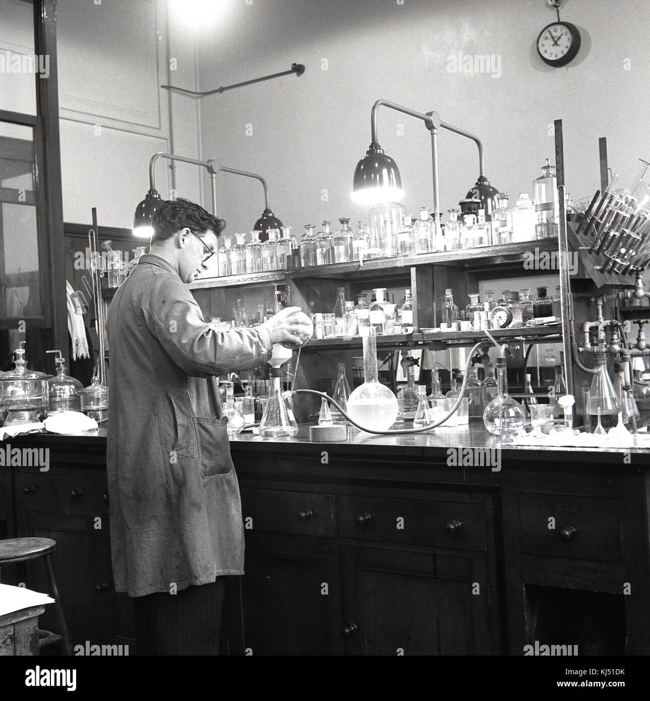1950s, historical, male research scientist working in a chemcial laboratory with numerous glass bottles and containers on the workbench. Stock Photo