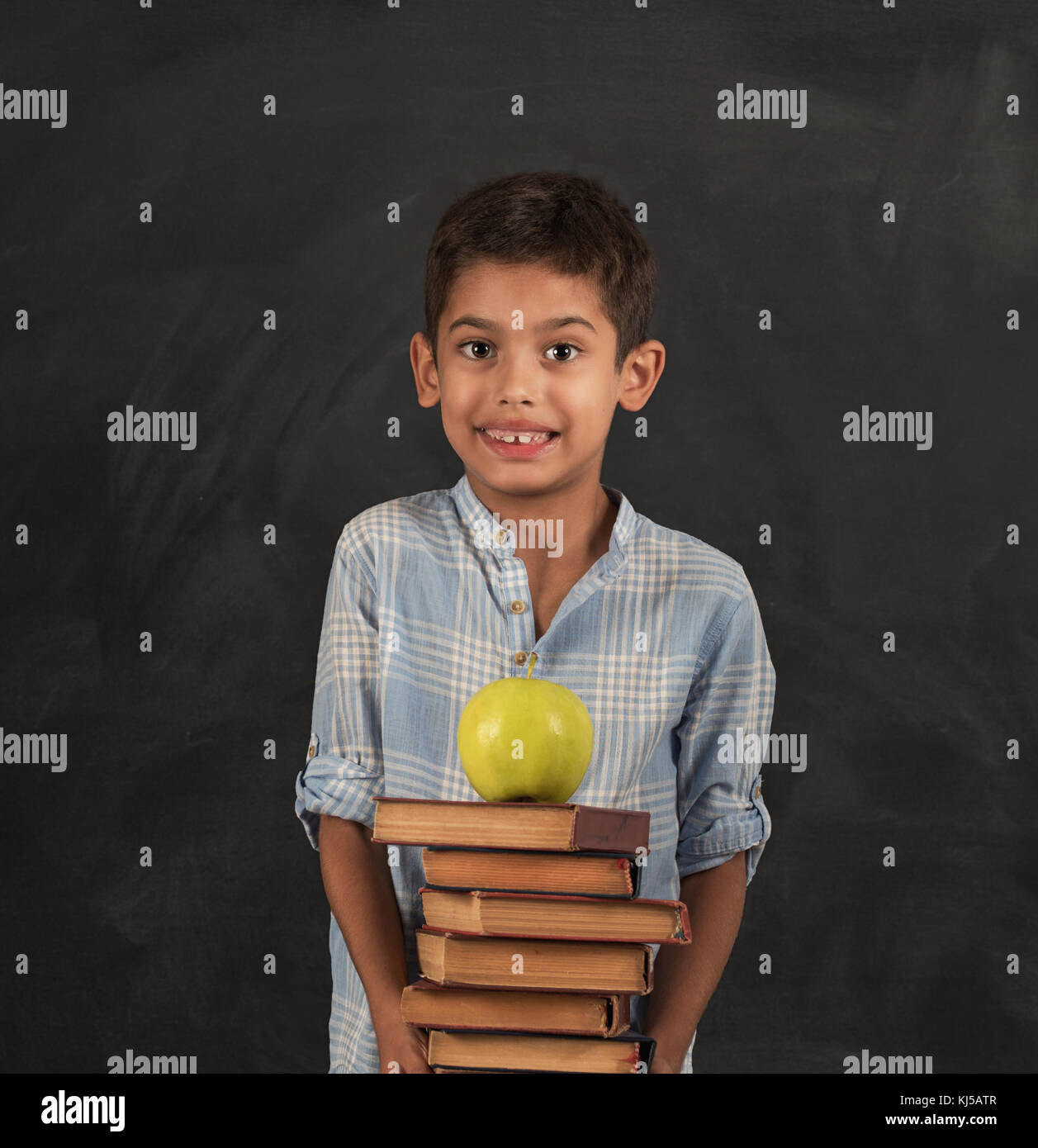 Closeup of little boy holding stack of books and apple. Happy schoolboy smiling and looking at camera. Stock Photo