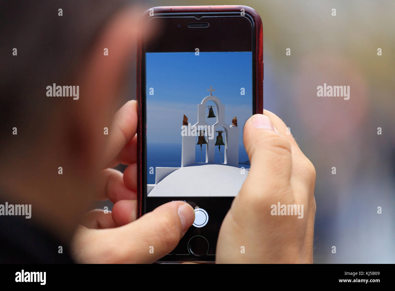 Greece, Santorini's church with bells picture appear on tablet, smartphone in man's hands. Blur background Stock Photo