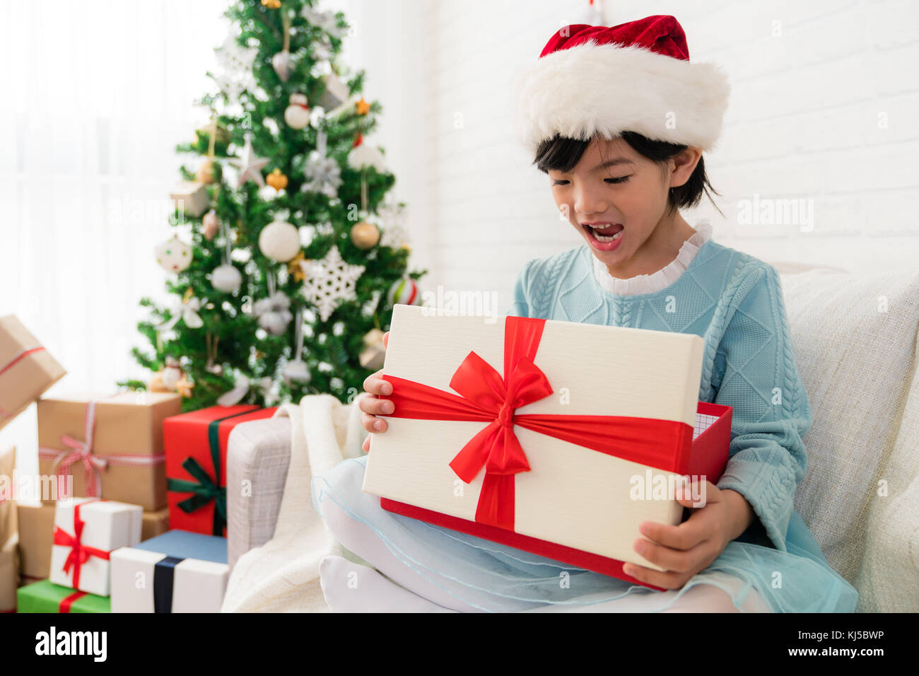 little cute Asian girl feel surprised face expression after she open the Christmas gift box sitting one sofa at home. Stock Photo