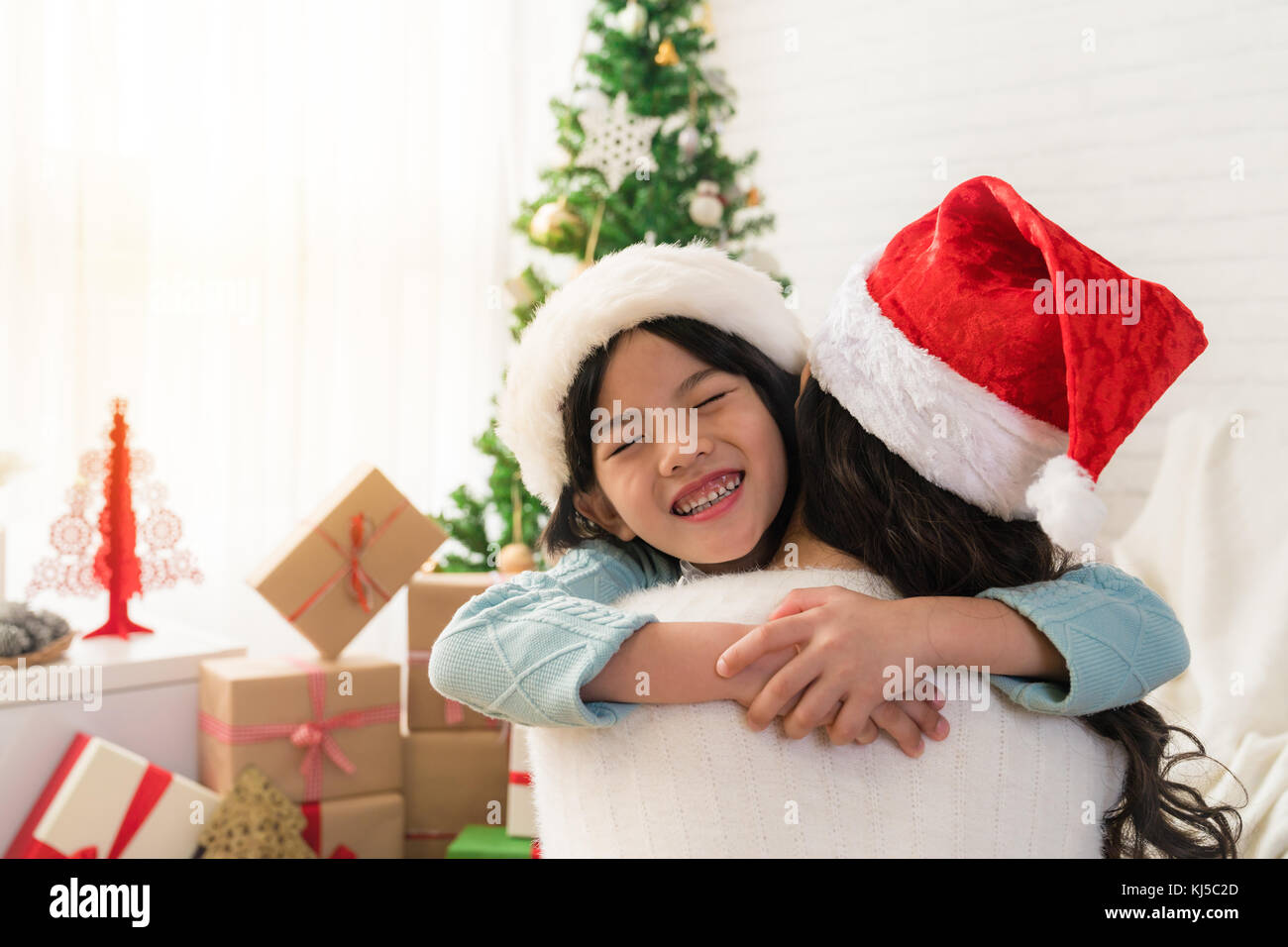 cute Asian daughter girl give her a mother hug after exchanging gifts.  Parent and little child having fun near tree indoors. Merry Christmas and  Happy Stock Photo - Alamy
