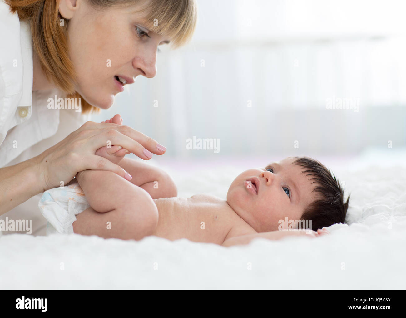 Mother and child on white bed. Parent and little kid relaxing at home. Mom doing massage baby. Stock Photo