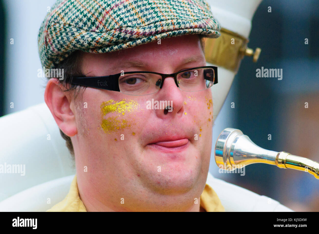 Male musician wearing glasses and a flat cap playing the sousaphone in the Carnival of The