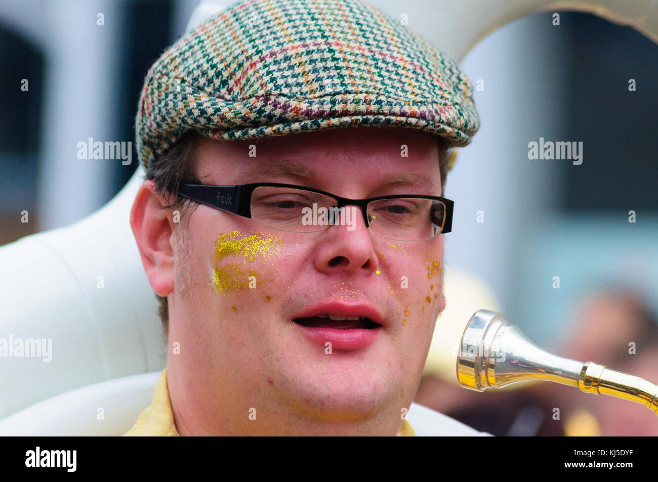 Male musician wearing glasses and a flat cap playing the sousaphone in
