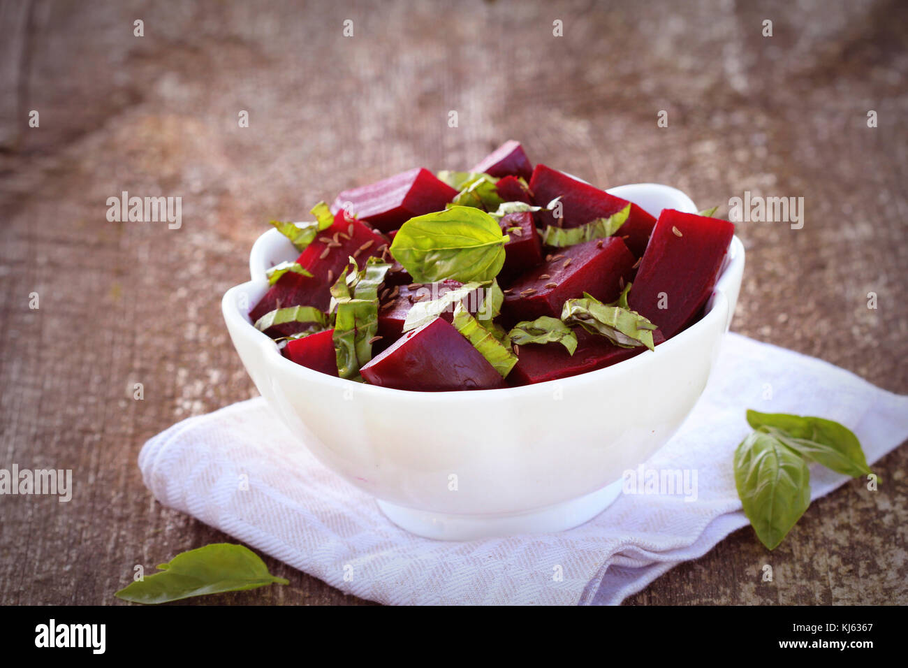 Healthy Beet Salad with fresh basil and dill seeds in bowl on rustic wooden table Stock Photo