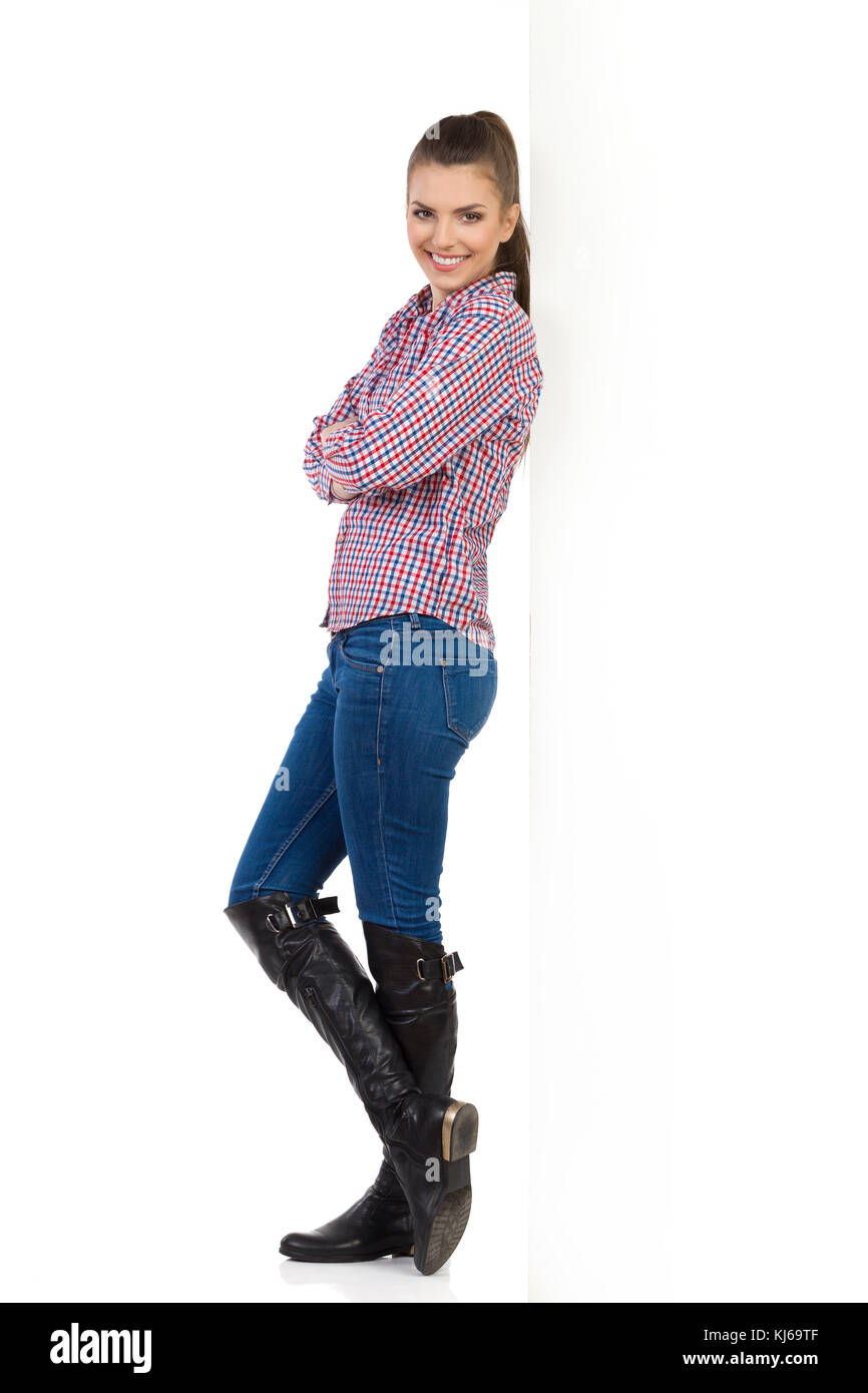 Young woman in jeans, black boots and lumberjack shirt leans with arms  crossed on white wall and looking at camera. Side view. Full length studio  shot Stock Photo - Alamy