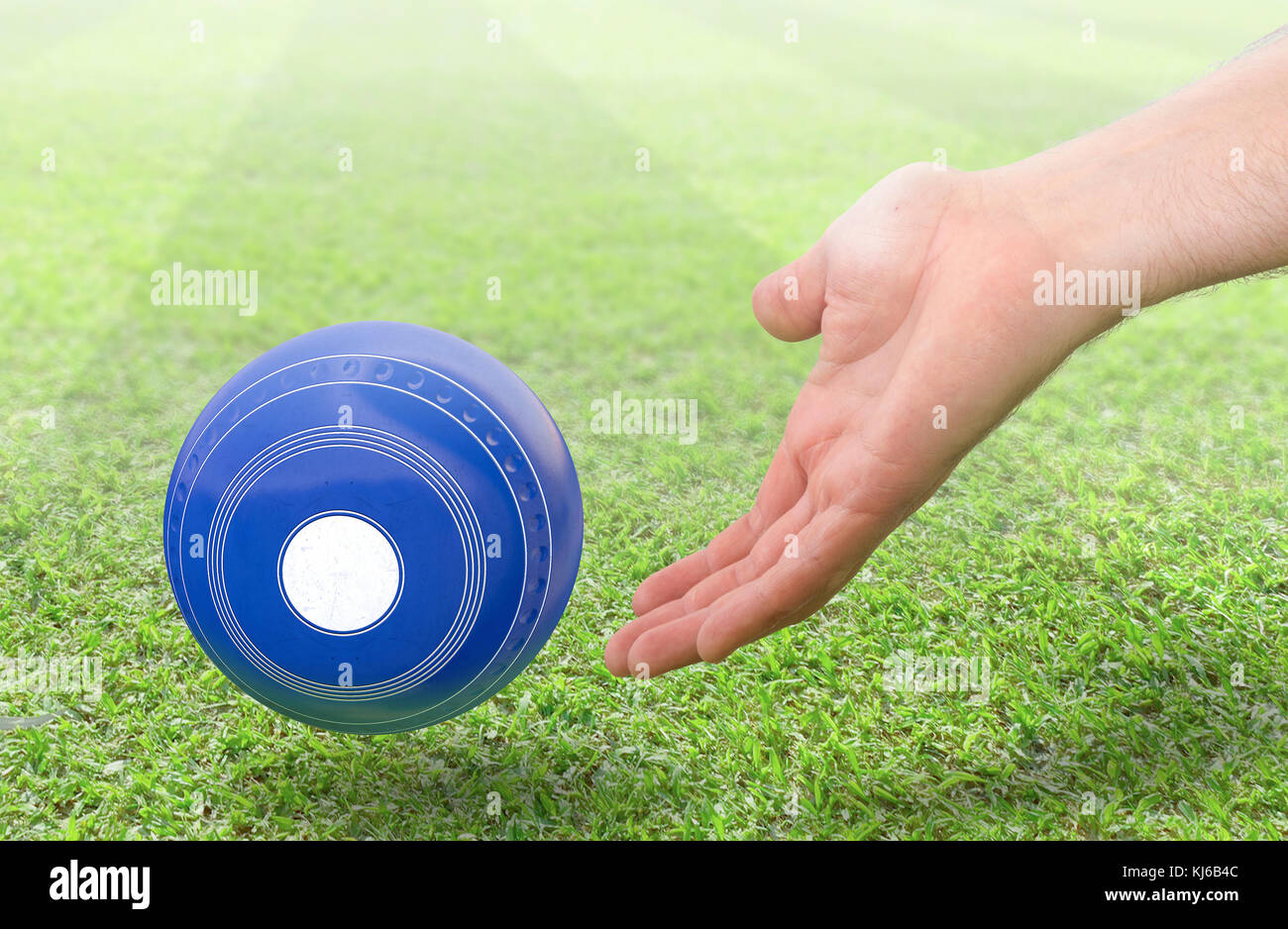 A male hand bowling and releasing a blue wooden lawn bowling ball on a green lawn grass surface -3D render Stock Photo