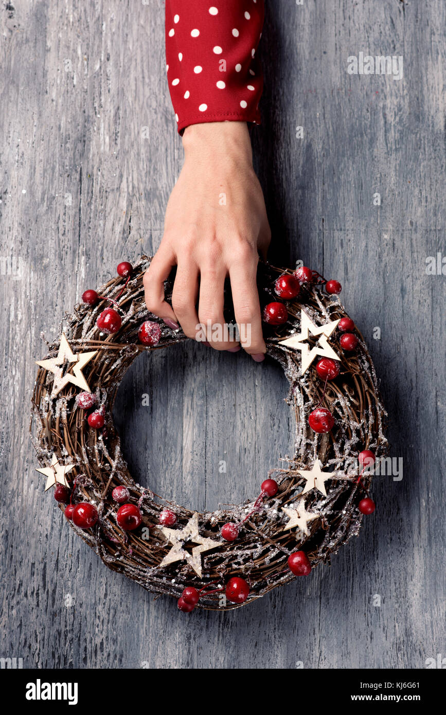 closeup of a young caucasian woman wearing a red dress patterned with white dots holding a christmas wreath in her hand on a gray rustic wooden surfac Stock Photo